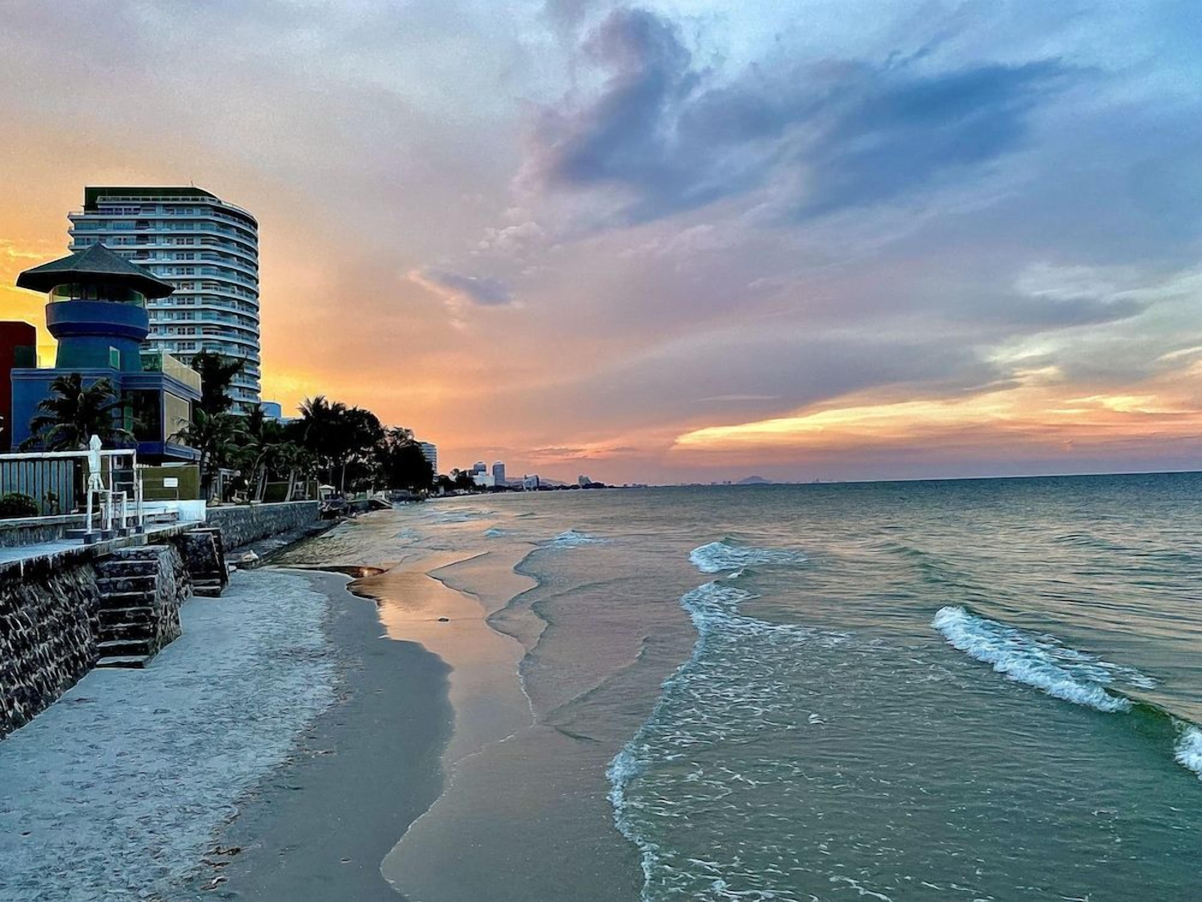 A beach with a curved hotel structure, a stone wall, and a sunset.