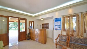 A reception area with a wooden reception desk, a sofa, and a bulletin board with information. - Birikos (Naxos)