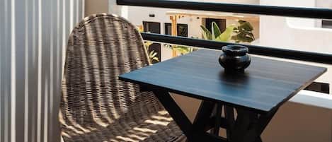 A balcony with wicker chairs and a table, overlooking a hotel building with a clear sky.