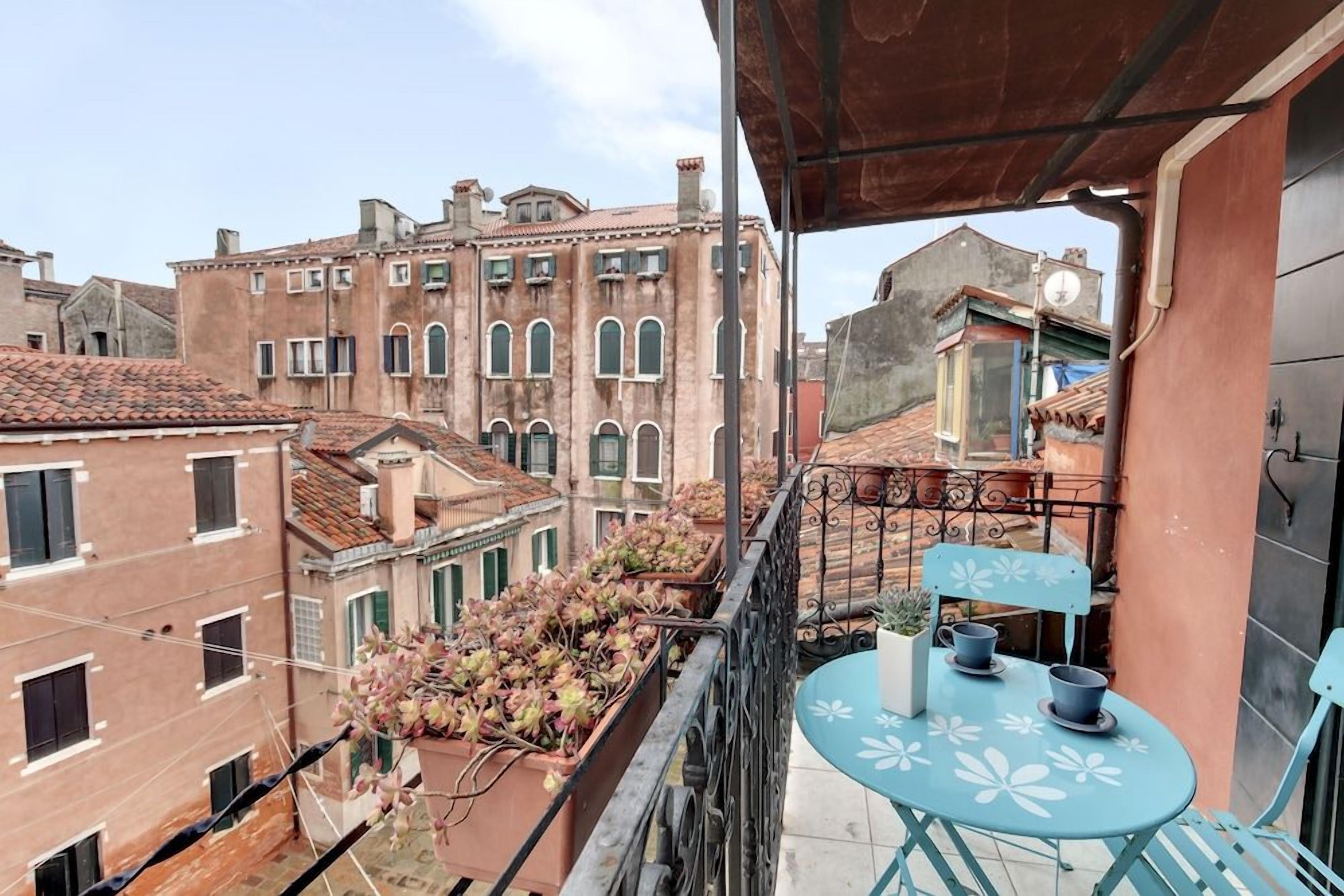 En balkon med et bord og stole, der udover bybillede med historiske bygninger.