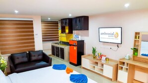 A hotel room with a bed, a sofa, a kitchenette, and a TV. - Ambrosial Suites (Pattaya)