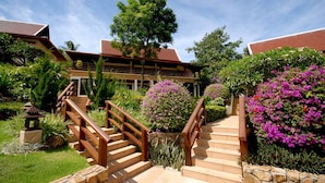 A hotel entrance with a wooden staircase, a stone wall, and lush greenery. - BKE Villa (Koh Samui)