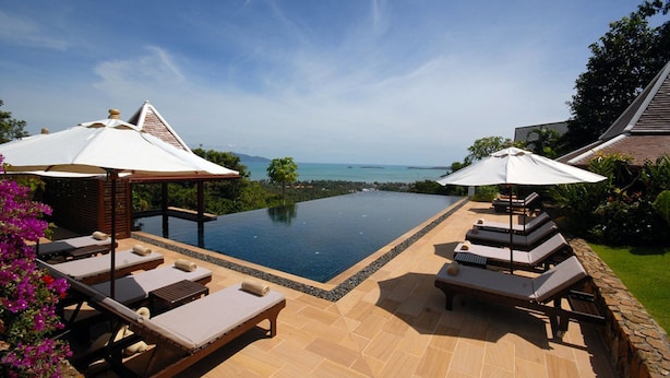 An infinity pool with lounge chairs and umbrellas, surrounded by greenery and a clear view of the ocean. - BKE Villa (Koh Samui)