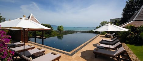 A infinity pool with lounge chairs and umbrellas, overlooking a body of water and greenery.