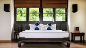 A bedroom with a bed, two nightstands, a window with a view of greenery, and a wall-mounted speaker. - BKE Villa (Koh Samui)