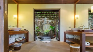 A bathroom with two sinks, a stone wall, a circular window, and a small waterfall feature. - BKE Villa (Koh Samui)