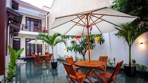 A courtyard with a round wooden table and chairs, surrounded by potted plants and a large umbrella. - Gia Phát (Da Nang Municipality)
