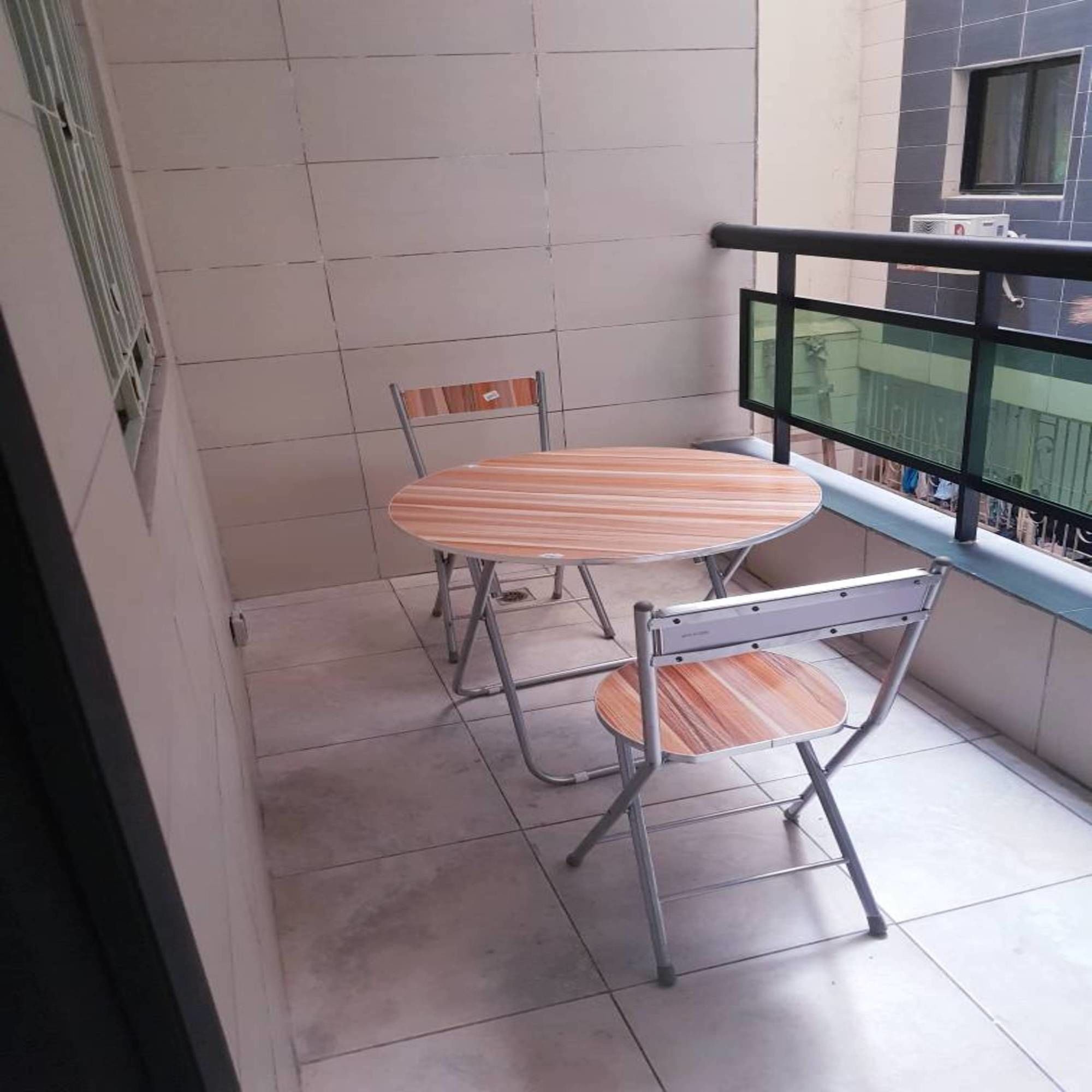 A balcony with a table and two chairs, a window with a view, and a metal railing.