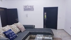 Ein Wohnzimmer mit einer Eckcouch, einem Glastisch und einer Tür.