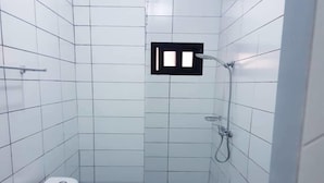 Ein kleines, schmales Badezimmer mit weißen Fliesen, einer Toilette, einem Waschbecken und einer Dusche.