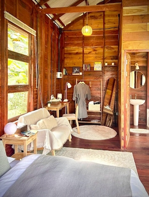 A cozy cabin interior with a bed, a desk, a chair, a hanging lamp, and a painting on the wall. - Katob Chaingdaw (Chiang Dao)