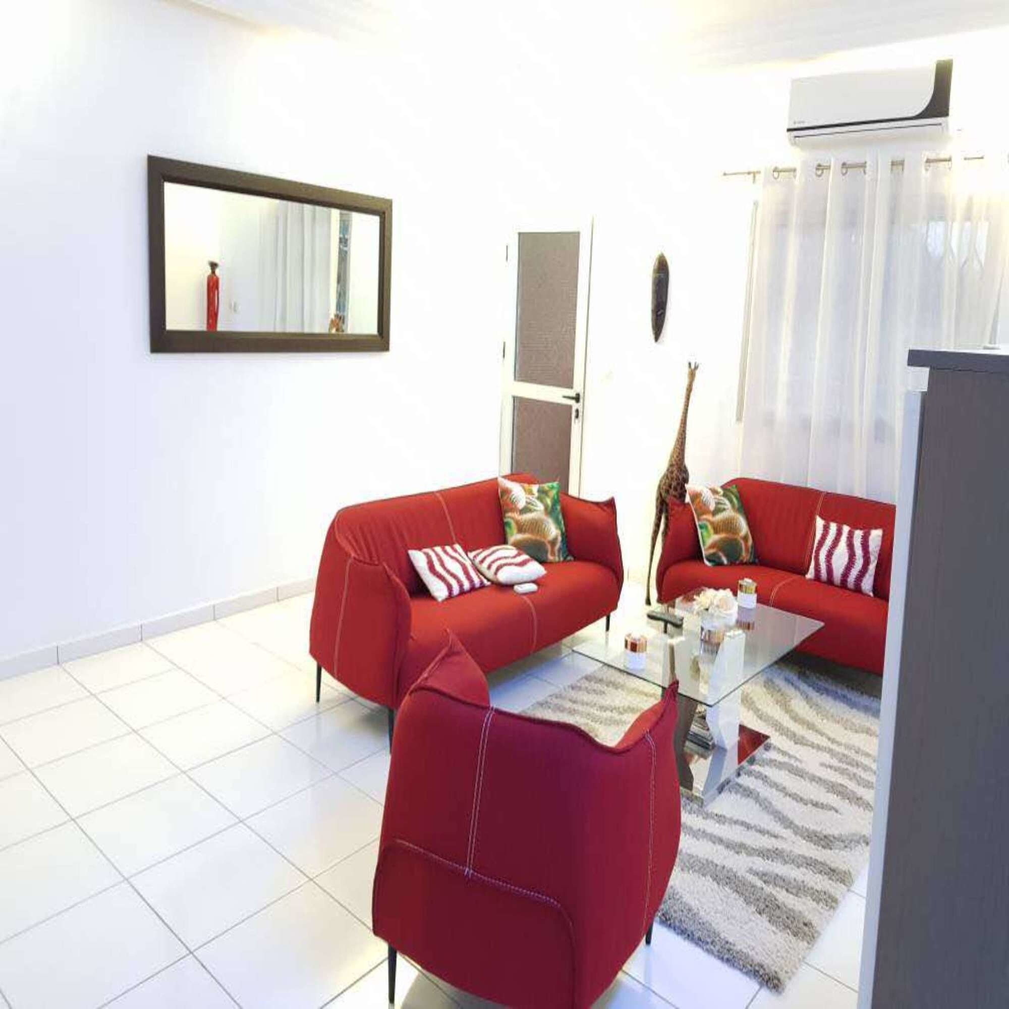 Una sala de estar con dos sofás rojos, una mesa de centro de vidrio, un espejo y un equipo de aire acondicionado blanco.