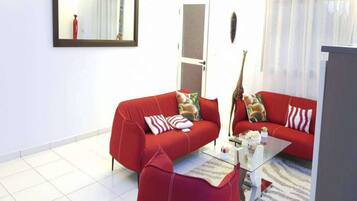 Una sala de estar con dos sofás rojos, una mesa de centro de vidrio, un espejo y un equipo de aire acondicionado blanco.