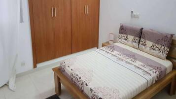 Un dormitorio con una cama de madera, una mesita de noche, un armario y una alfombra estampada.