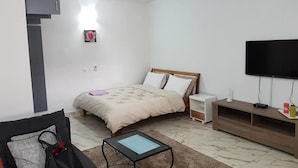 A hotel room with a bed, bedside tables, a TV, a small table, and a chair. - Studio Arcade (Abidjan)