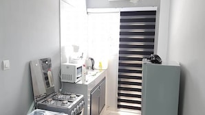 A compact kitchen with a gas stove, microwave, and a refrigerator. - Studio Arcade (Abidjan)