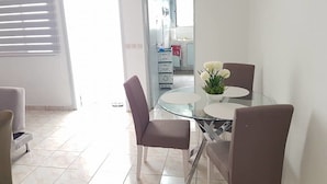 A dining area with a glass table and chairs, a potted plant, and a view into the kitchen. - Résidence Petite Villa (Abidjan)