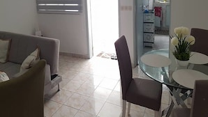 A living area with a sofa, a glass table, and a chair. There is a door leading to a kitchen area. - Résidence Petite Villa (Abidjan)