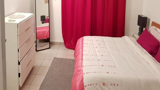 A bedroom with a bed, a dresser, a mirror, and a red curtain. - Résidence Petite Villa (Abidjan)