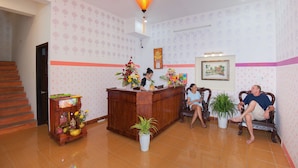 A reception area with a wooden desk, a reception desk, a staircase, and a wall with patterned wallpaper. - Tri Tran Homestay (Da Nang Municipality)