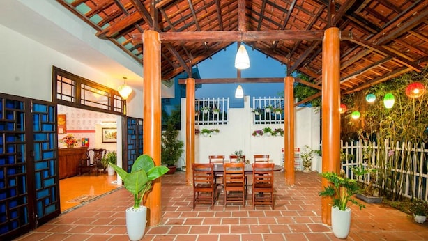 An outdoor patio with a brick floor, wooden chairs, and potted plants. - Tri Tran Homestay (Da Nang Municipality)