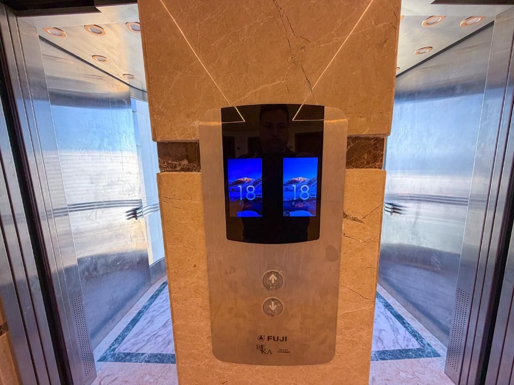 Een lift met een digitaal scherm waarop het cijfer 10 staat, het merk 'FUJI' en twee knoppen: één omhoog en één omlaag.