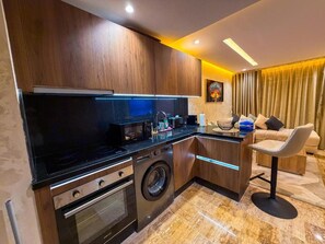 Uma cozinha moderna com máquina de lavar embutida, sala de jantar com balcão e área de estar com sofá e cadeira.