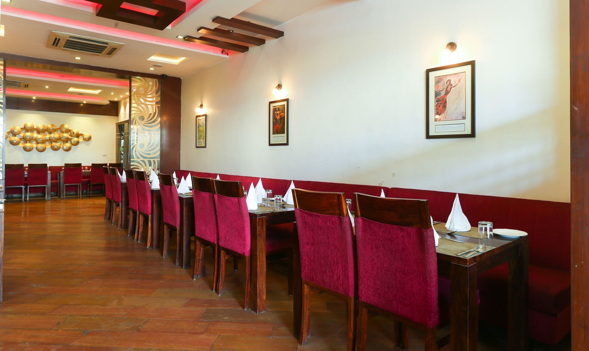 A restaurant with a long dining area, red upholstered chairs, and a wall with framed artwork.
