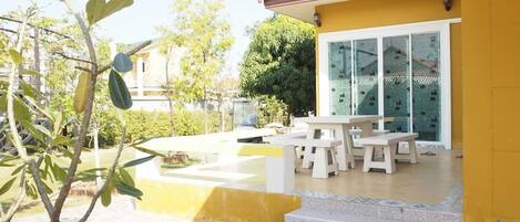 Un patio con mobiliario exterior, un pequeño árbol y un edificio de techo con tejas.