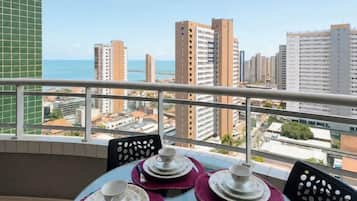 Varanda com mesa posta para refeições, vista para paisagem urbana com edifícios e um corpo d'água.