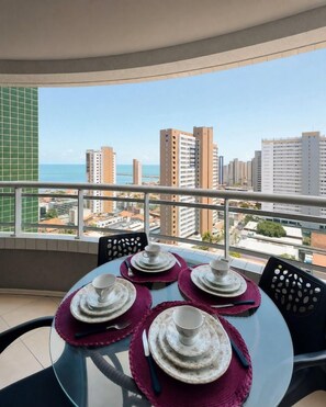 Varanda com mesa posta para refeições, vista para paisagem urbana com edifícios e um corpo d'água.