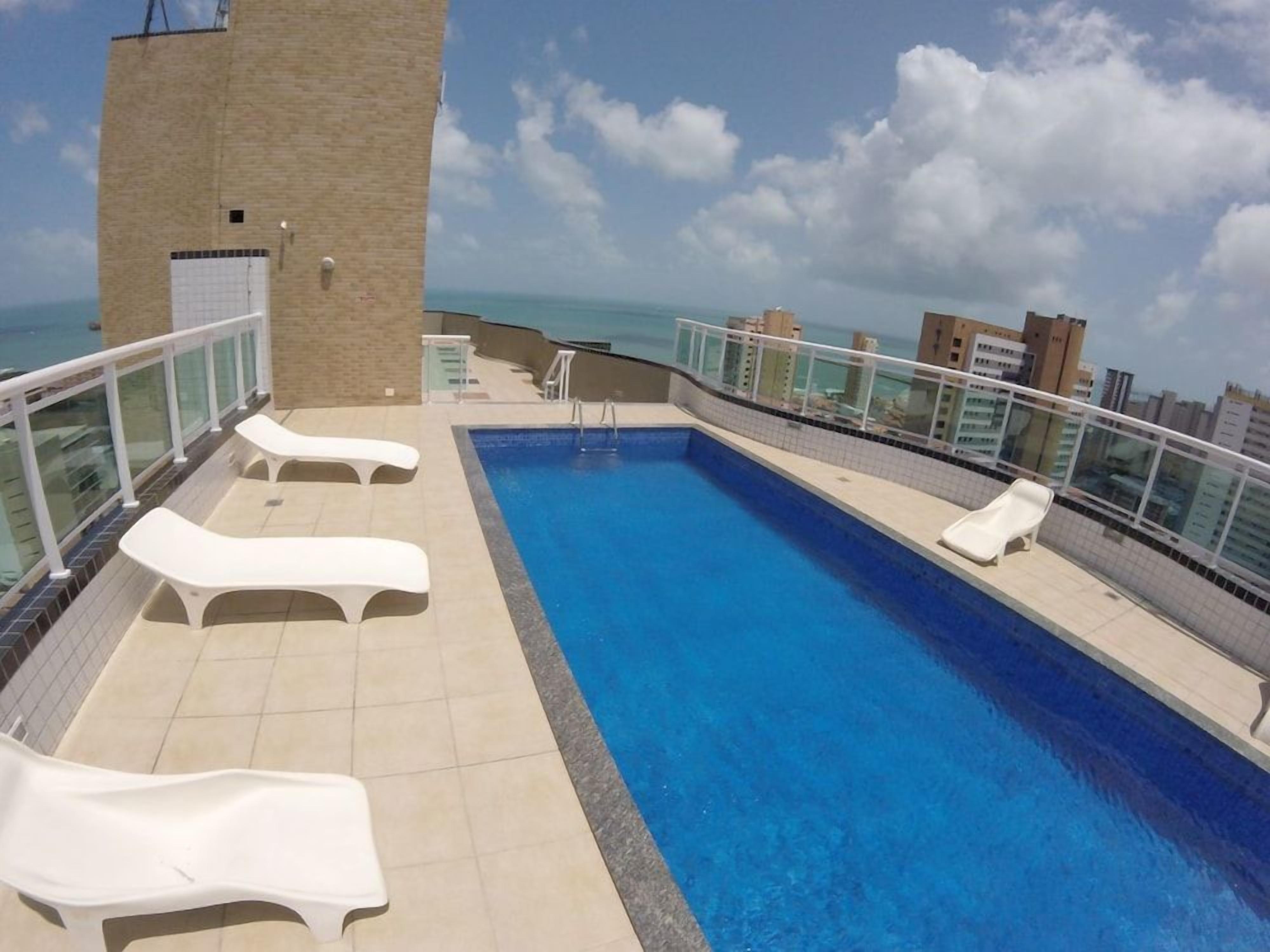 A rooftop pool with lounge chairs and a view of the ocean.