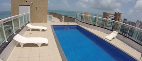 A rooftop pool with lounge chairs and a view of the ocean.