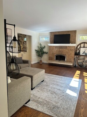 A modern living room with a sectional sofa, a fireplace, and a television mounted above it. - 5bdr / House along the creek (Kelowna)