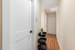 A narrow hallway with white doors, a small plant on a black stand, and a wooden floor.