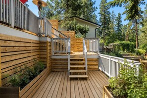 Eine Holzterrasse mit einer Treppe, die zu einem überdachten Bereich führt, umgeben von viel Grün und Bäumen.