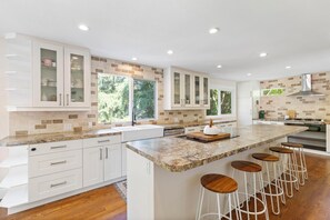 Una cocina moderna con armarios blancos, encimera de granito y una isla central con taburetes de bar.