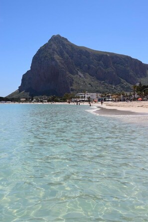 A beach with clear water, a mountain in the background, and a few buildings along the shore. - Affittacamere Agosta (San Vito Lo Capo)