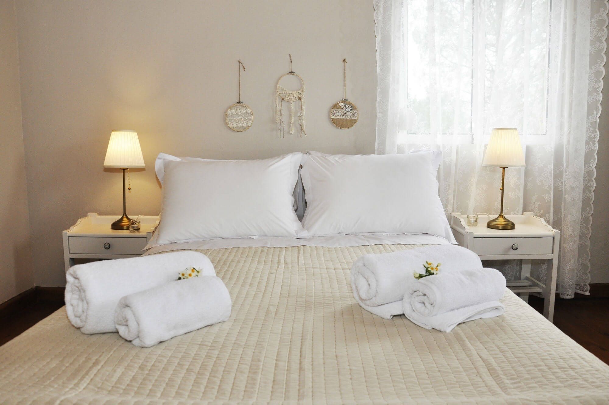 Un letto rifatto con due cuscini, due comodini con lampade e due asciugamani con fiori.