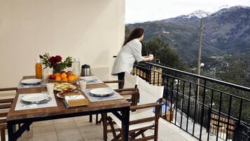 Una tavola imbandita per la colazione, una persona accanto alla ringhiera e vista su un paesaggio montuoso.