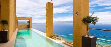 An infinity pool with a clear view of the ocean, surrounded by beige pillars and potted plants.