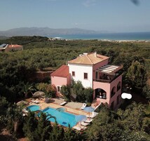 Ένα διώροφο σπίτι με πισίνα, περιτριγυρισμένο από πράσινο και με θέα σε μια παραθαλάσσια περιοχή.