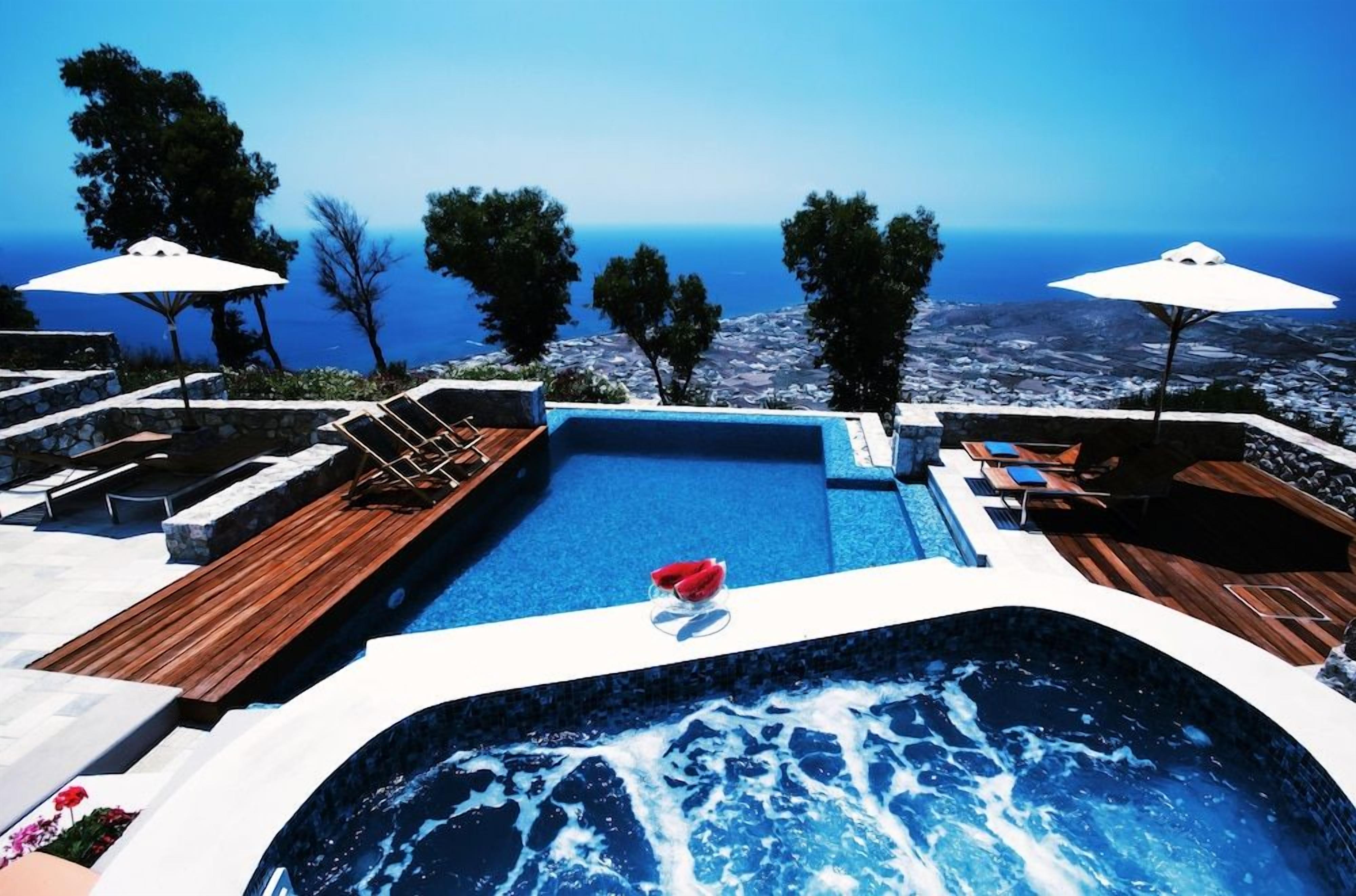 A swimming pool with a view of the sea, surrounded by lounge chairs and umbrellas.