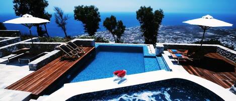 A swimming pool with a view of the sea, surrounded by lounge chairs and umbrellas.