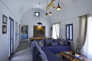 A living room with a sofa, a coffee table, and a dining area with a table and chairs. - Villa Asterope, Luxury Retreat by Pleiades (Santorini)