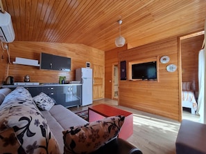 A modern interior with a wooden ceiling, a sofa, a television, and a kitchen area. - Sunset Pansiyon & Apartments (Kemer)