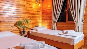 A wooden cabin room with two beds, a potted plant, and a window with curtains. - Bungalowsky (Kemer)