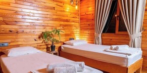 A wooden cabin room with two beds, a potted plant, and a window with curtains. - Bungalowsky (Kemer)
