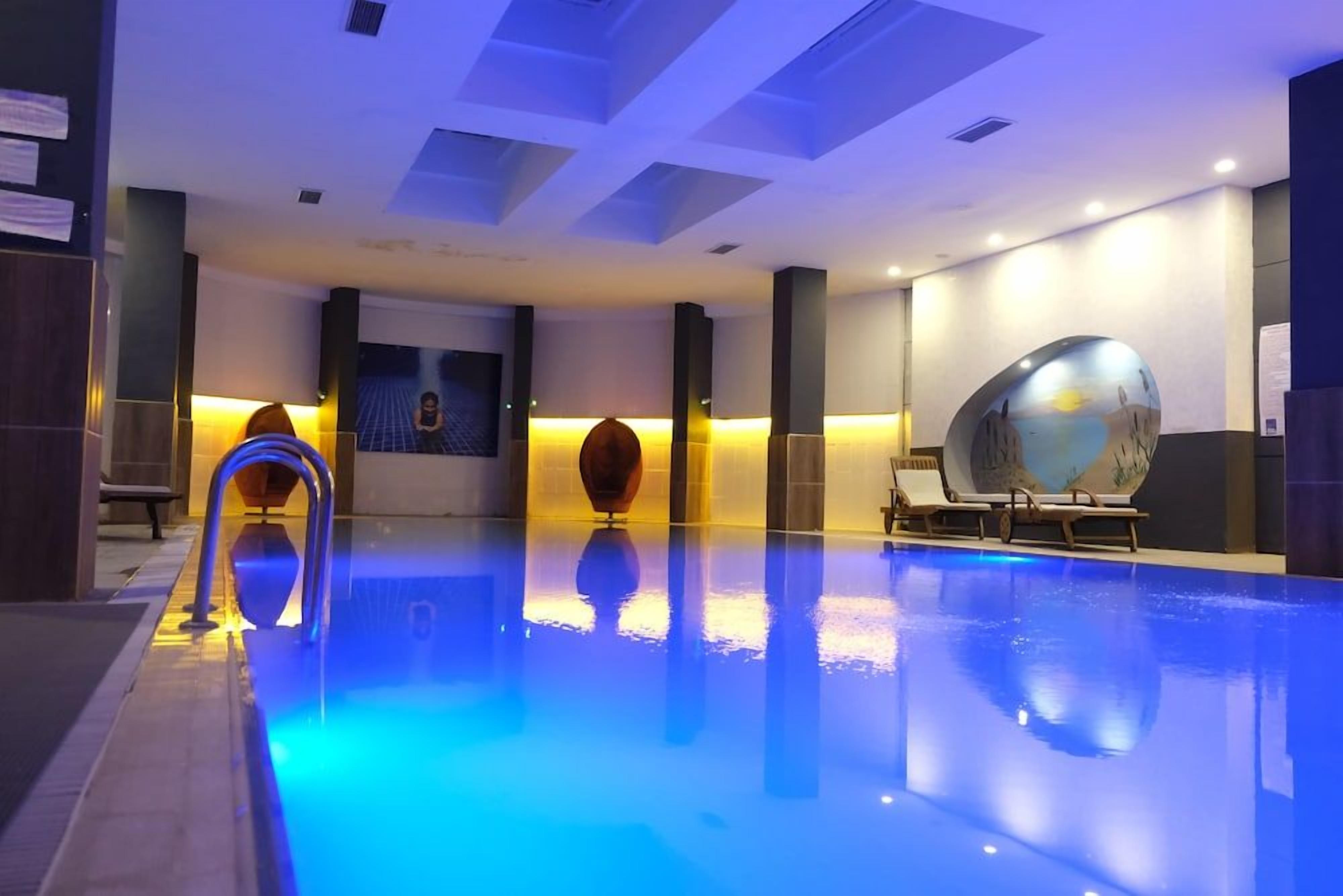 A swimming pool with a blue-lit edge, a sun-shaped water feature, and lounge chairs.