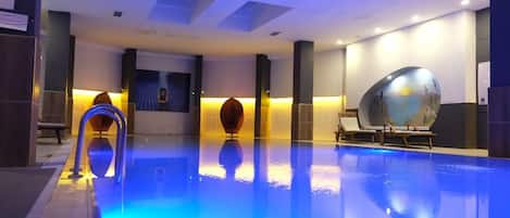A swimming pool with a blue-lit edge, a sun-shaped water feature, and lounge chairs.